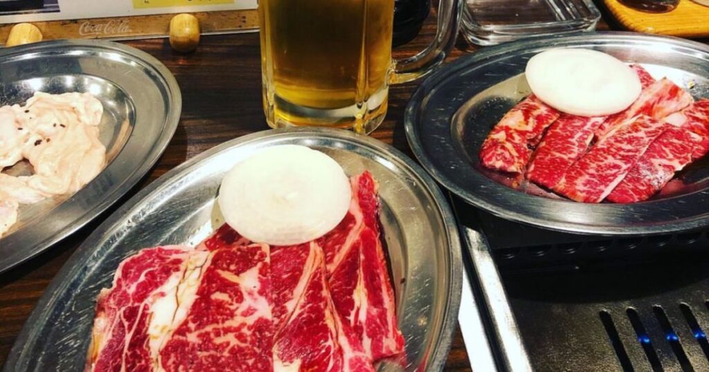 焼肉屋さんのテーブルに、たくさんの肉（ロース、カルビ、ホルモン）のお皿と、生ビールのジョッキが置かれた写真。