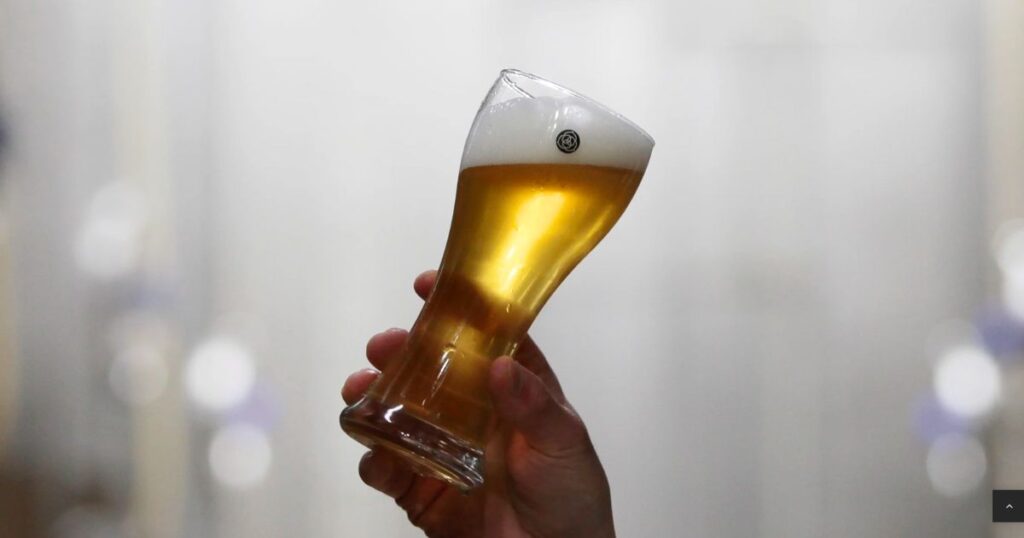 コエドビールのロゴマークが入ったグラスに注がれたビールを持つ手。