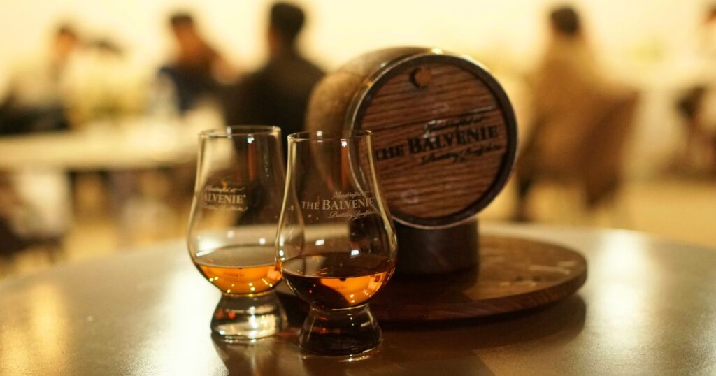 「THE BALVENIE」のロゴが焼印されたミニチュアの樽の前に、ウイスキーが注がれたテイスティンググラスが２つ。