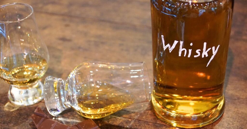 ウイスキーのテイスティンググラスが２つ。
「WHISKY」と書かれたボトル。
飲み比べのイメージ写真。